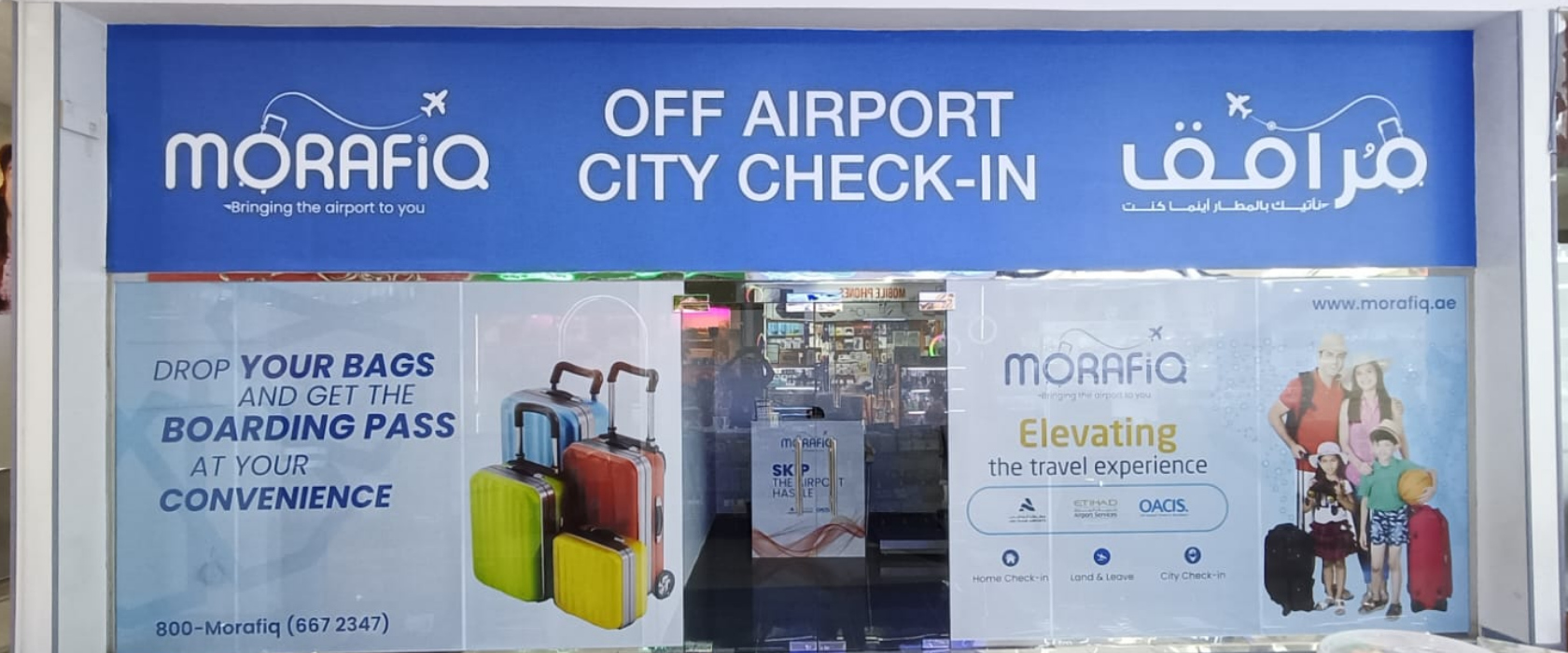 Image of a storefront labeled "Morafiq" offering off-airport city check-in services. The window display includes multiple luggage bags and a sign reading, "Drop your bags and get the boarding pass at your convenience." The colors are primarily blue and white.